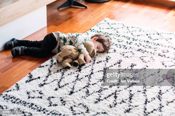 diagonal photo of a child sleeping on the floor at home with part of his body on the carpet. he is hugging his stuffed dog. - chien en peluche photos et images de collection