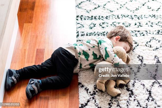 side shot of a boy who has fallen asleep on the floor at home, with part of his body on the carpet. he is hugging his stuffed dog. - leksakshund bildbanksfoton och bilder