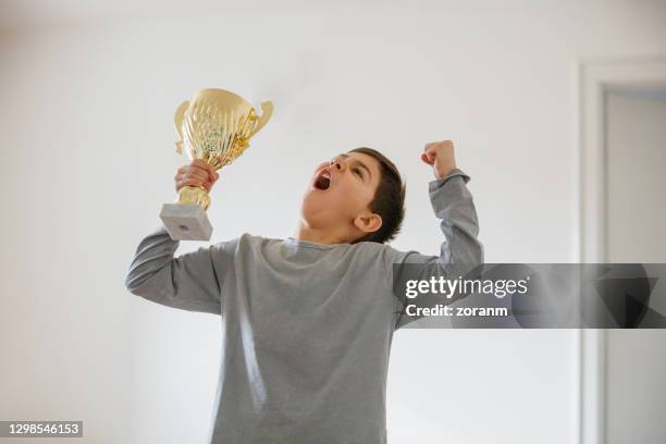 boy imagining success, raising arms with golden trophy and shouting - awards inside stock pictures, royalty-free photos & images