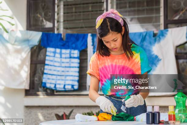 若いアジアの女の子は自宅でネクタイ染料の服を作って楽しむ - tie dye ストックフォトと画像