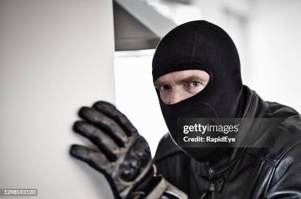 gruseliger mann maskiert von schwarzer balaclava und mit leder bekleidet sieht furios und erschrocken aus: möglicher einbrecher - skimaske stock-fotos und bilder