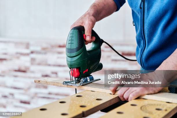 detail view of an unrecognizable man cutting a piece of wood with a jig saw. concept of do-it-yourself, woodworking and carpentry at home. - serra tico tico serra elétrica - fotografias e filmes do acervo