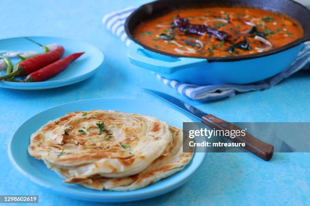 image of indian butter chicken / tikka curry served in turquoise blue cooking pan filled with large chunks of chicken breast meat in curry sauce with garnish of red onion slices and mustard seeds, lachha paratha (layered flatbread), red chilli . - parantha stock pictures, royalty-free photos & images