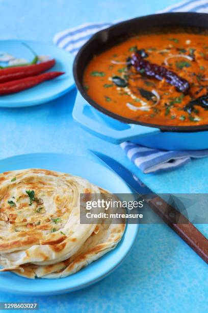 image of indian butter chicken / tikka curry served in turquoise blue cooking pan filled with large chunks of chicken breast meat in curry sauce with garnish of red onion slices and mustard seeds, lachha paratha (layered flatbread), red chilli . - parantha stock pictures, royalty-free photos & images