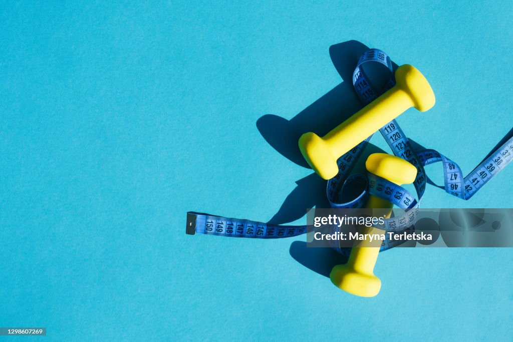 Yellow kettlebell for sports exercise with a centimeter on a blue background.
