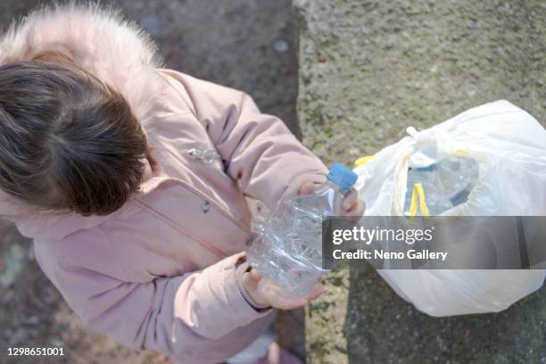 little girl holding a plastic bottle next to a garbage bag - reciclar stock pictures, royalty-free photos & images