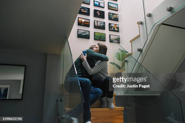 couple having a cuddle on the stairs after a 'bad news' phone call - emotional support stock pictures, royalty-free photos & images