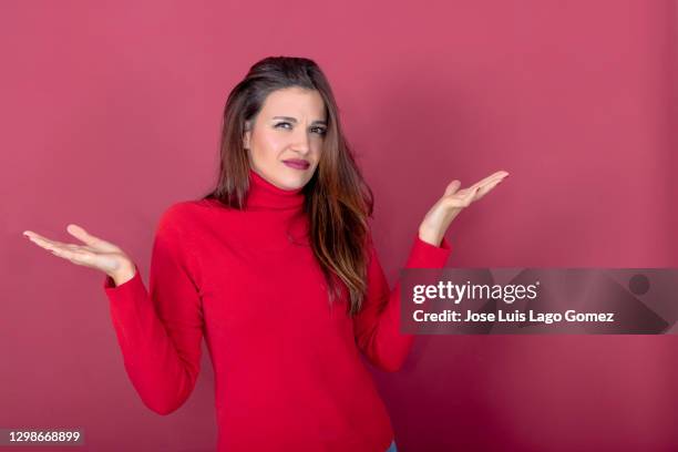 young beautiful woman dressed in red turtleneck sweater, with open arms palms up and gesture of disagreement or not understanding - disgusto foto e immagini stock