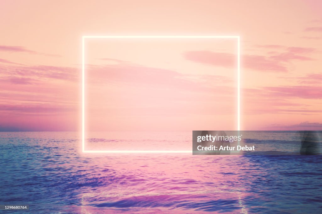 Neon square installation glowing over the sea at sunset.