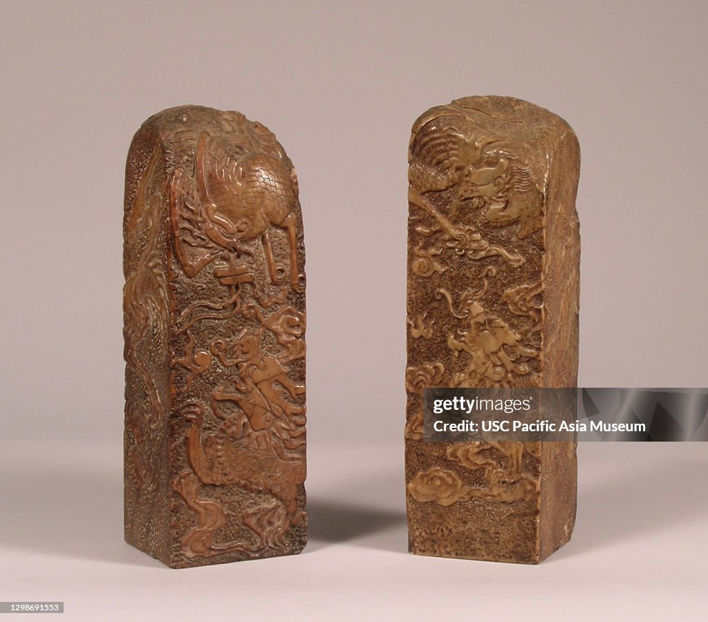 Pair of mottled brown soapstone seals with design of phoenix bird flying over a dragon chasing the flaming pearl