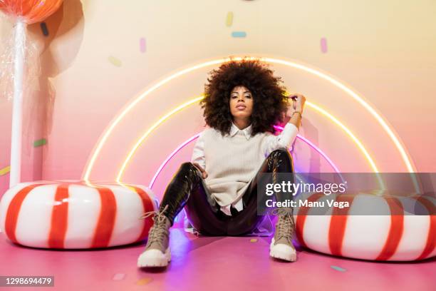 afro woman sitting next to huge candies. - sweet shop stock-fotos und bilder