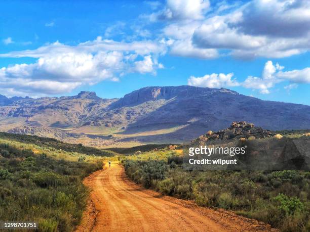 picturesque cycling mountain biking downhill on gravel road towards the mountains with clouds freedom - south africa stock pictures, royalty-free photos & images