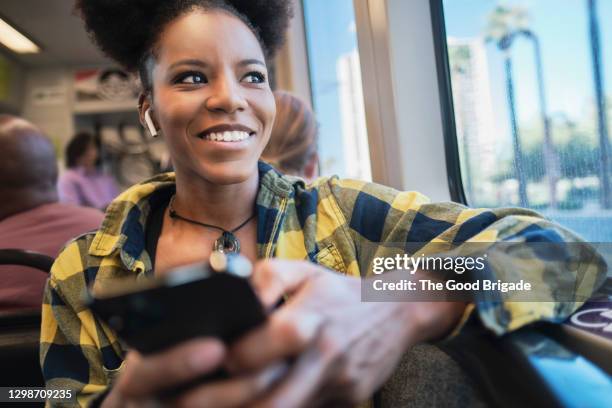 mid adult woman smiling while looking out window of bus - in ear headphones photos et images de collection