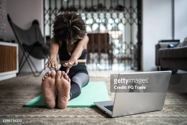 自宅でラップトップでストレッチと運動をする若い女性 - 前屈運動 ストックフォトと画像