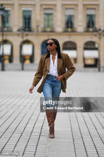 Emilie Joseph wears sunglasses, a khaki military jacket from Saint-Laurent YSL, a white shirt / blouse from Zara with ruffled collar, blue denim...