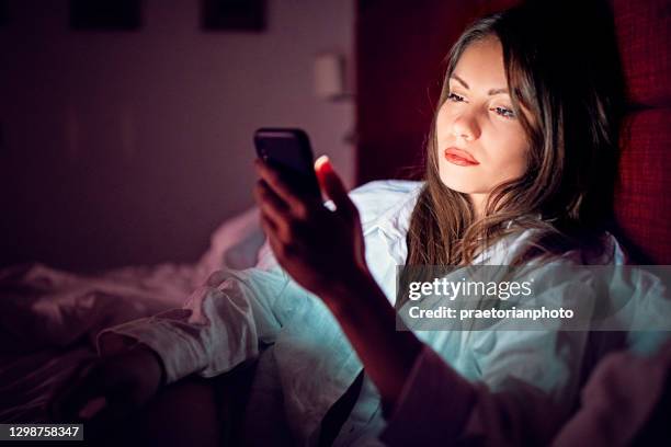 la mujer está enviando mensajes de texto en la cama por la noche - cheating wives photos fotografías e imágenes de stock