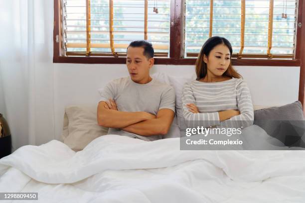 portrait of stressed young adult asian wife on bed along with husband in bedroom interior background. couple turning away from each other. marriage and bad relationship life concept. - bed conflict stock pictures, royalty-free photos & images