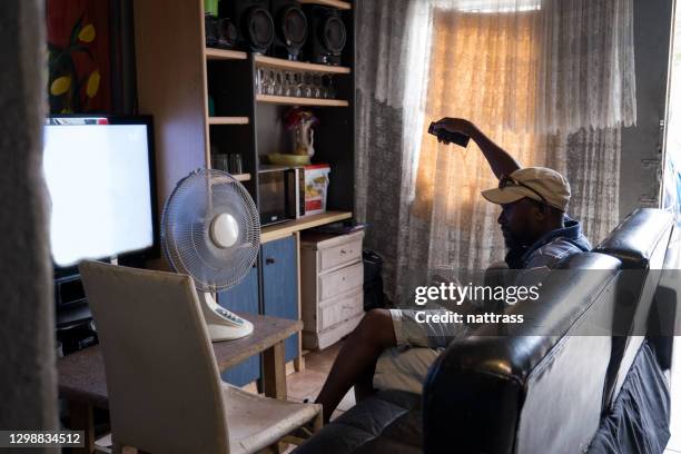 homem africano senta no sofá e assiste um pouco de televisão - township - fotografias e filmes do acervo