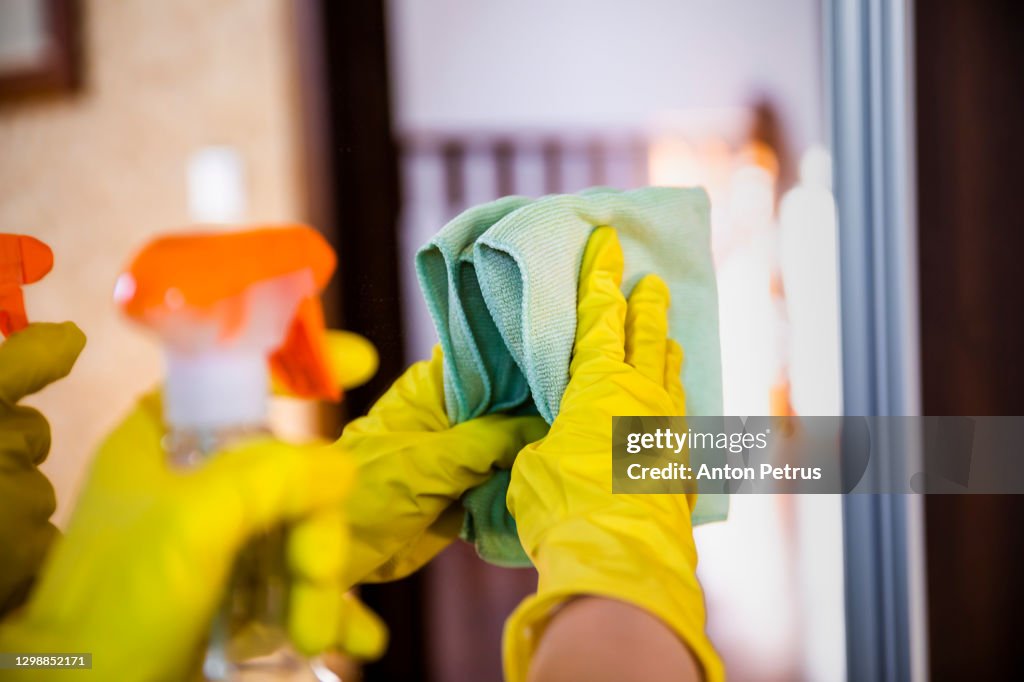 Woman in rubber gloves wipes the mirror in the room