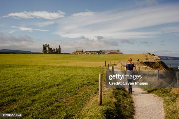 woman walking along path between whitby and robinshood bay with - whitby stock-fotos und bilder