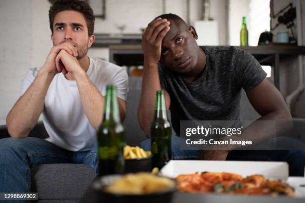 unhappy diverse friends watching disappointing football match - television set stock-fotos und bilder