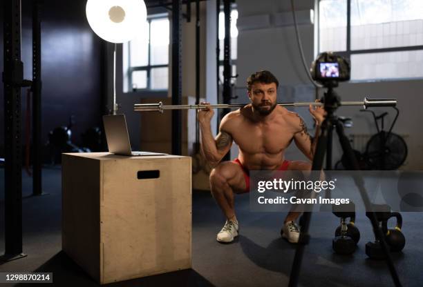 sportsman doing squats with bar in front of camera - hombre agachado fotografías e imágenes de stock