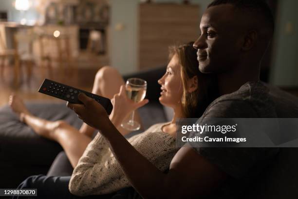 multiethnic couple with wineglass watching tv - couple night stock-fotos und bilder