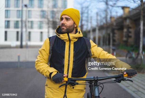 portrait of a young man, wearing winter clothes, walking in the city, beside his bicycle. - winter cycling ストックフォトと画像