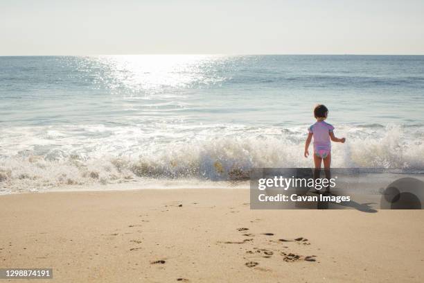 a little girl stands at the edge of the shore with oncoming wave - bethany beach stock pictures, royalty-free photos & images