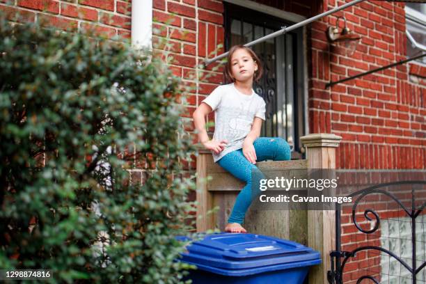 a small fierce girl with serious gaze sits on fence with hole in pants - damaged fence stock pictures, royalty-free photos & images