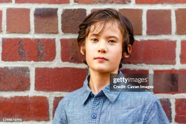 a serious beautiful boy leans back on brick wall with a direct gaze - 12 ears stock pictures, royalty-free photos & images