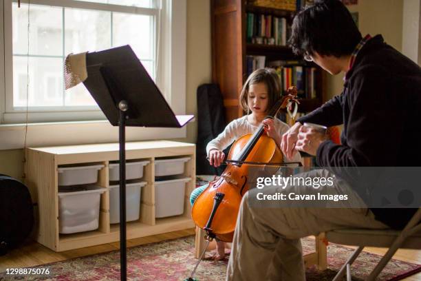 a father helps little girl practice cello at home by window - cello - fotografias e filmes do acervo