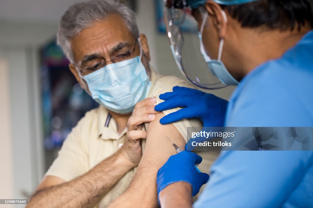 Doctor injecting vaccine into arm of senior male patient