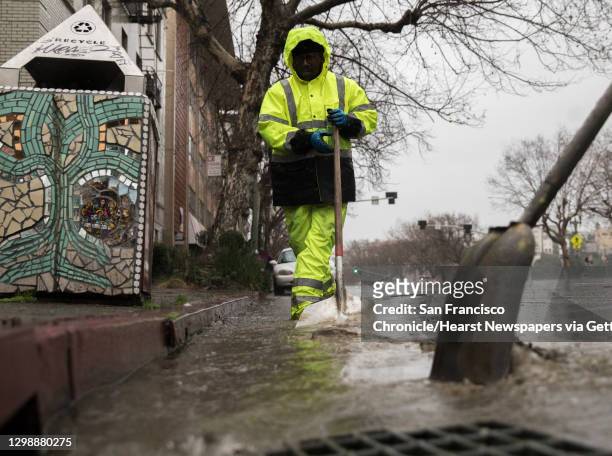 Employees with the Oakland Public Works drainage department work to unclog storm drains along Grand Avenue as heavy rains pour in Oakland, Calif....