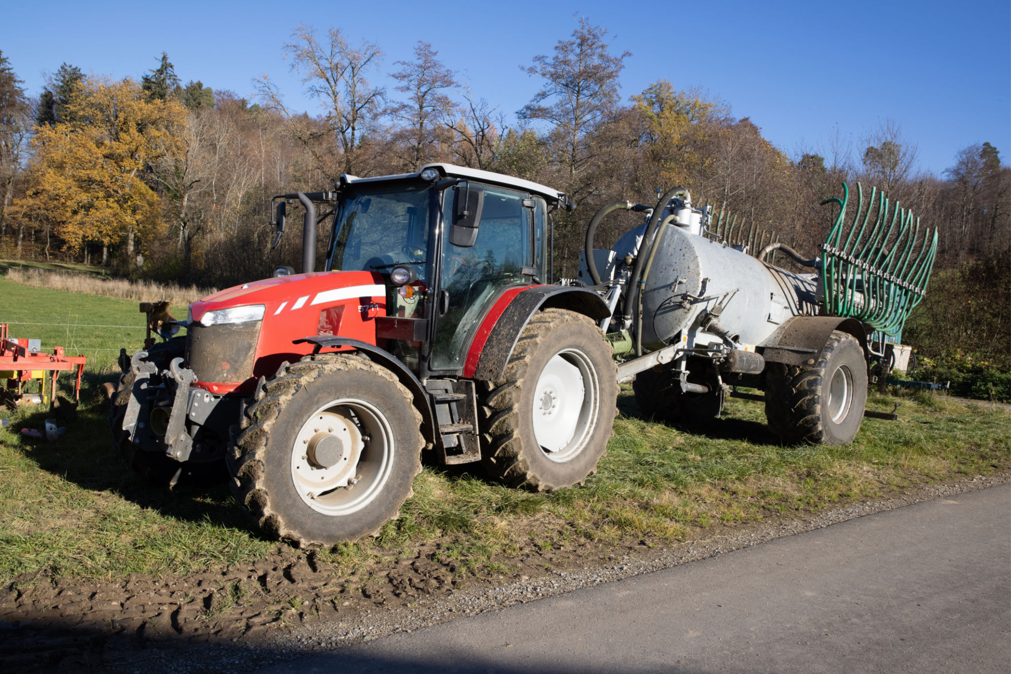 red tractor with slurry tanker and green hoses stands on an autumn meadow, the field can be cultivated faster with these machines, during the day , sunshine without clouds red tractor with slurry tanker and green hoses stands on an autumn meadow, the field can be cultivated faster with these machines, during the day , sunshine without clouds