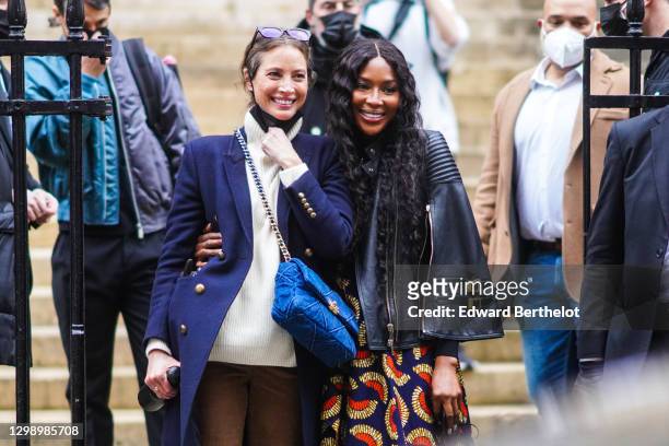 Naomi Campbell is seen wearing a black leather biker jacket, a blue and red dress with printed patterns, black pants ; Christy Turlington wears...