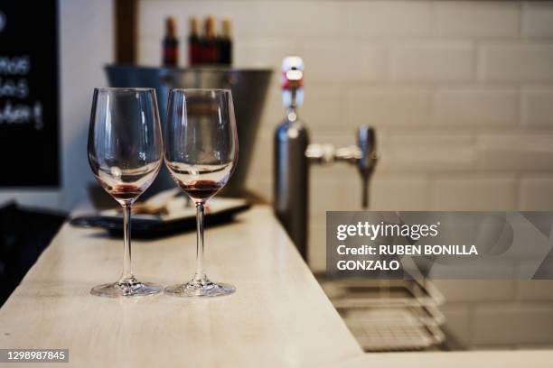 front view of two empty crystal wine glasses on a bar table with a metallic bucket with some opened wine bottles with cork and a beer faucet without jar at the back. horizontal photography. - empty glasses after party stock-fotos und bilder