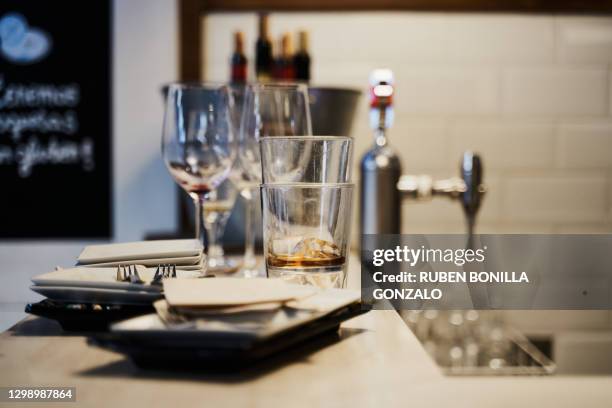 front view of dirty empty crystal wine glasses, plate, napkin and fork on a bar table with a metallic buckt with some opened wine bottles with cork and a beer faucet without jar at the back. horizontal photography. - dirty glass stock pictures, royalty-free photos & images