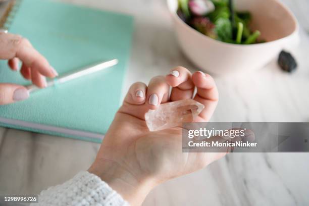 hand of woman holding healing crystals with notebook in background - healing crystals stock pictures, royalty-free photos & images