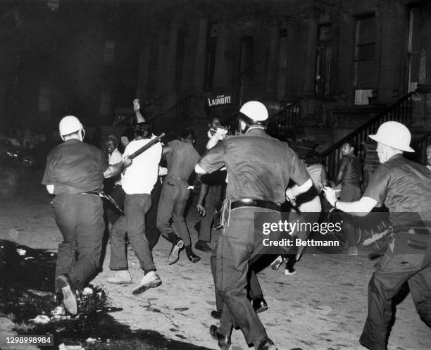 Helmeted, club-swinging police officers disperse a violent crowd on a Harlem street here during riots July 18th following a demonstration protesting...