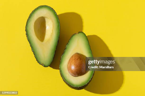 avocado halves with trendy hard light and hard shadow on yellow background - avocado isolated imagens e fotografias de stock