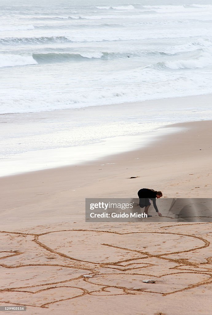 Women drawing hearts into wet beach sand.