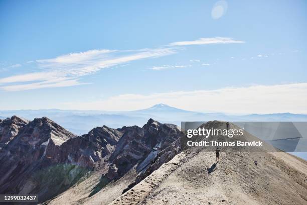 hikers climbing ridgeline at mt st helens with mt adams in background - mount st helens stock-fotos und bilder