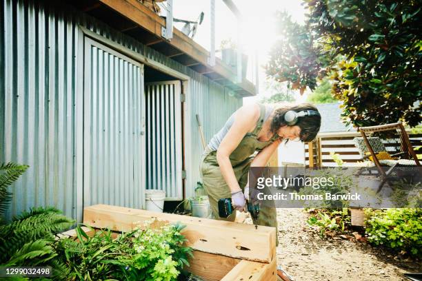 woman building raised garden beds in backyard on summer afternoon - working tools foto e immagini stock