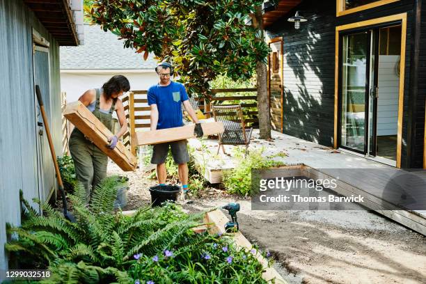 couple carrying lumber to build raised garden beds in backyard - home improvement stock pictures, royalty-free photos & images