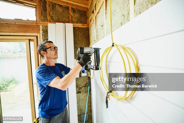 man using nail gun to install siding during home remodeling project - gun wall photos et images de collection
