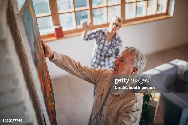 casal de idosos em sua nova casa pendurando uma pintura juntos - pendurando - fotografias e filmes do acervo