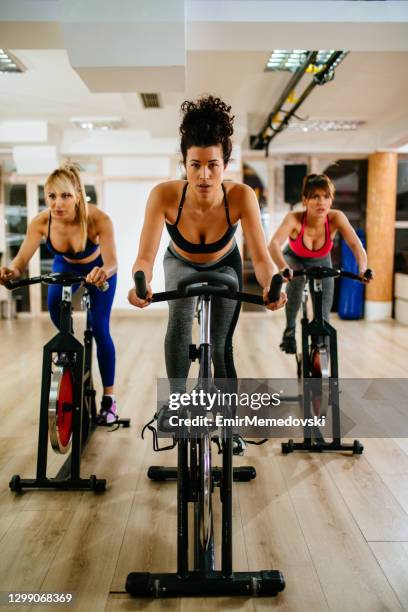 sporty women exercising on exercise bike at modern gym - spinning stock pictures, royalty-free photos & images