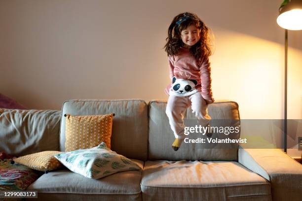 happy four years old little girl jumping on the couch on pajamas - royalty free stock-fotos und bilder