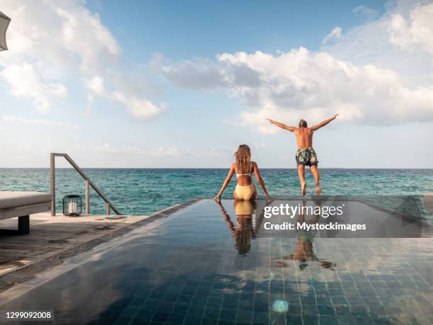 couple enjoying luxury vacations, man jumping from pool to sea - infinity pool stock pictures, royalty-free photos & images